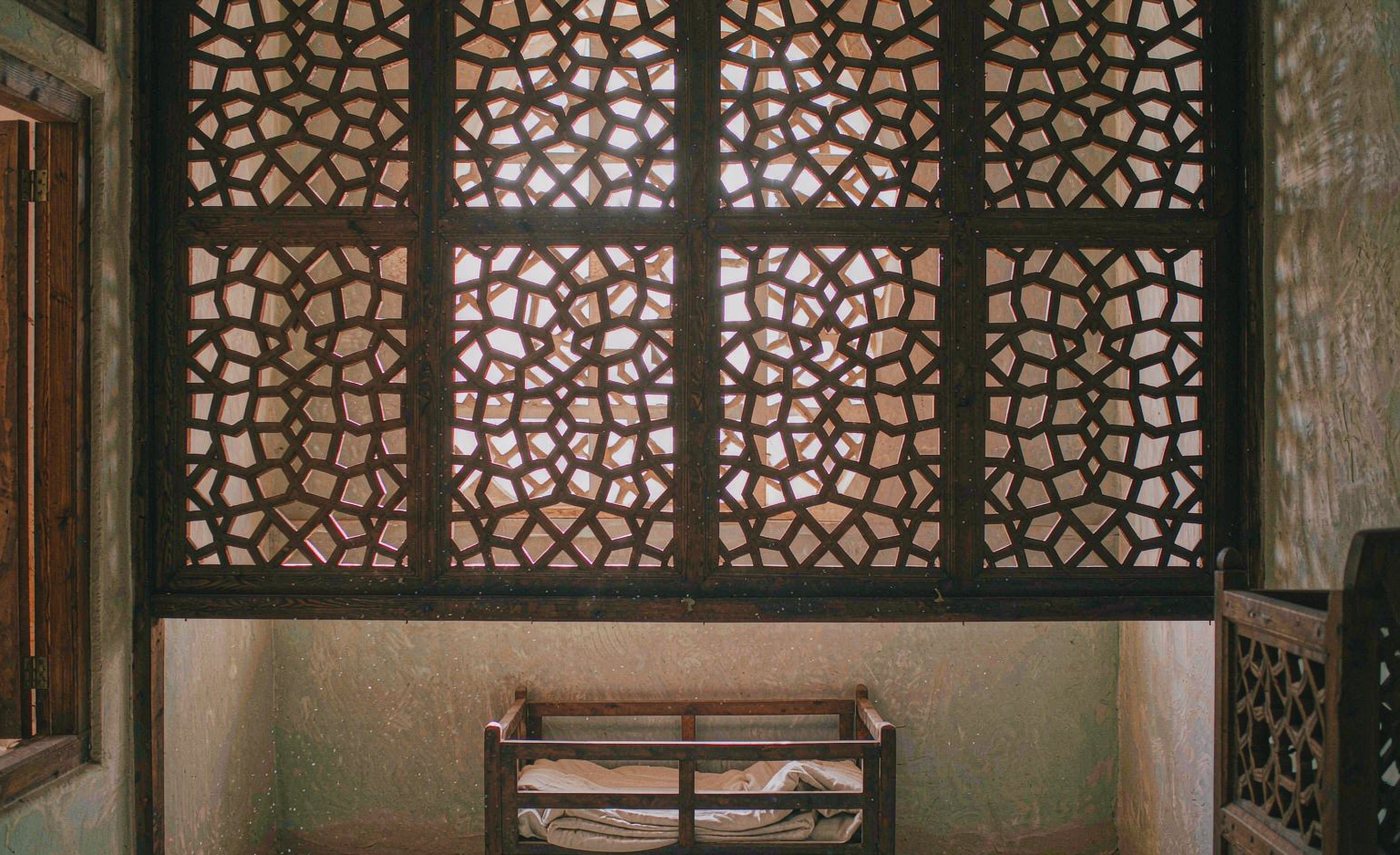 Sunlight through a mashrabiya screen above a wooden crib